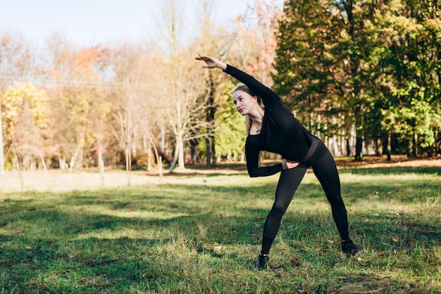 La ragazza in abiti sportivi neri esegue l'inclinazione di esercizio lasciata all'aperto, il giorno di autunno.