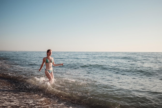 La ragazza in bikini corre lungo le onde sulla spiaggia in estate