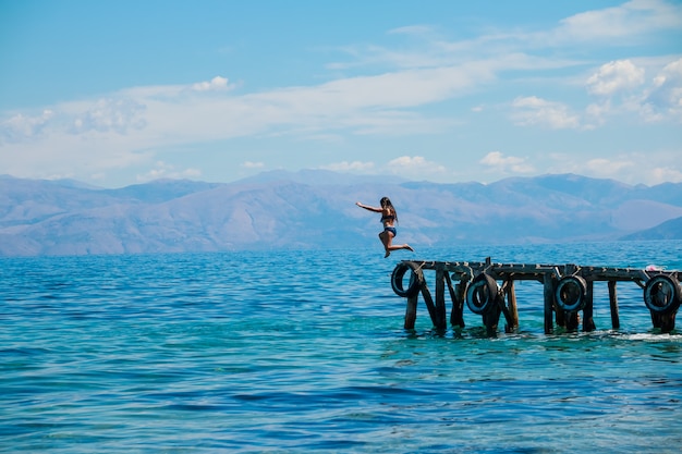 La ragazza in buona salute sportiva sta saltando giù dal pilastro nel sea.jumping dal pilastro nell&#39;acqua.