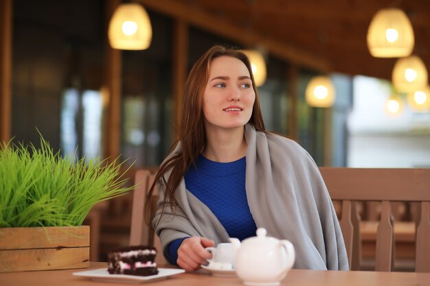 La ragazza in caffè si siede e beve il tè con il dessert