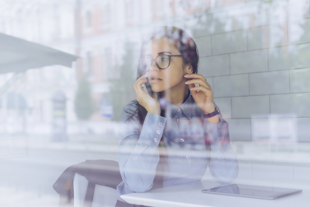 La ragazza in camicia blu e occhiali sta parlando al telefono, seduta in un caffè