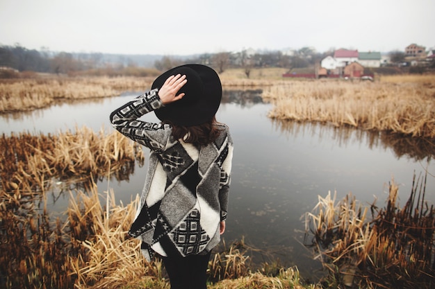 La ragazza in cardigan grigio posa sulla riva di un lago. Vista posteriore