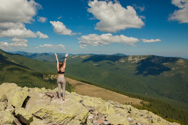 La ragazza in cima alla montagna alzò le mani Ampia vista sulle montagne estive all'alba e una catena montuosa lontana coperta Concetto di bellezza della natura