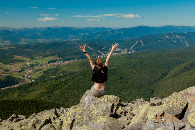 La ragazza in cima alla montagna sollevò le mani. Ampio Mountain View estivo ad alba e distanti catena montuosa coperta. Bellezza della natura