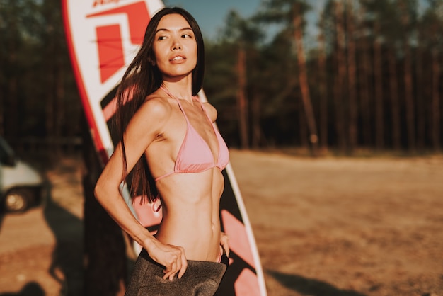 La ragazza in costume da bagno rosa sta accanto a praticare il surfing sulla spiaggia.