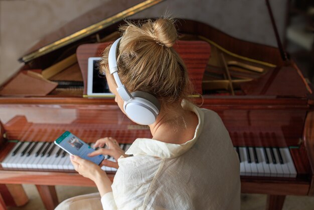 La ragazza in cuffia suona un pianoforte antico e usa uno smartphone per studiare