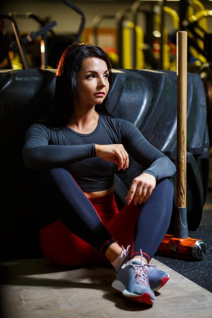 La ragazza in palestra con una mazza in mano si siede vicino a una grande ruota