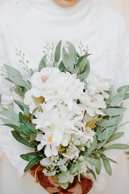 La ragazza in un abito da sposa bianco tiene tra le mani un mazzo di fiori.