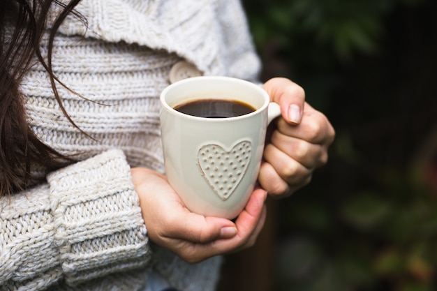 La ragazza in un accogliente maglione lavorato a maglia beve caffè dalla tazza