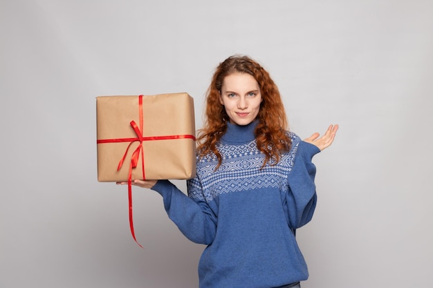 La ragazza in un maglione sta tenendo un regalo su un fondo bianco