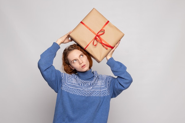 La ragazza in un maglione sta tenendo un regalo su un fondo bianco