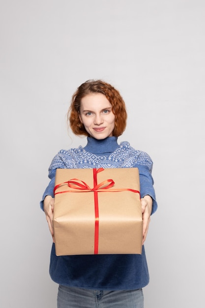 La ragazza in un maglione sta tenendo un regalo su un fondo bianco