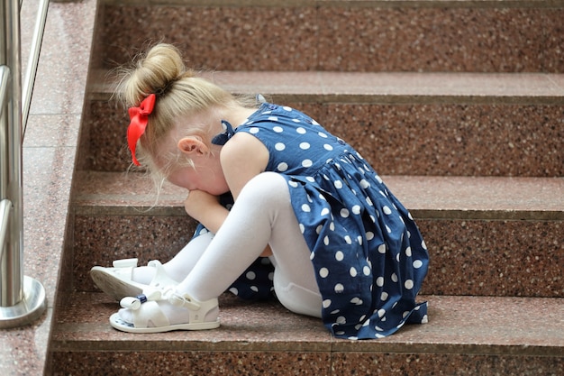 La ragazza in un vestito blu si siede sui gradini e piange