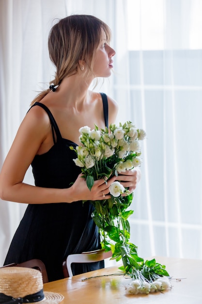 la ragazza in un vestito nero sta tenendo le rose bianche prima di metterle in un vaso