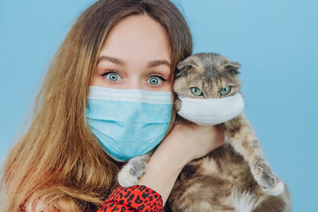 La ragazza in un vestito rosso con una mascherina medica sulla sua faccia tiene un gatto.