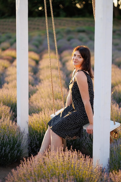 La ragazza in un vestito si siede su un'altalena in un campo di lavanda