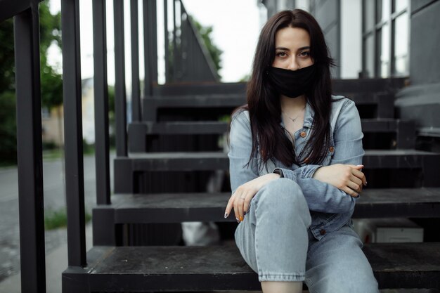 La ragazza in una maschera protettiva su un balcone guarda una città vuota