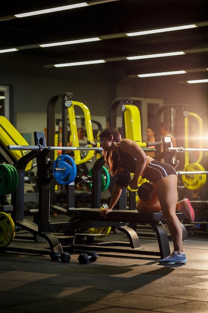 La ragazza in una tuta sportiva nera esegue un esercizio con manubri in palestra