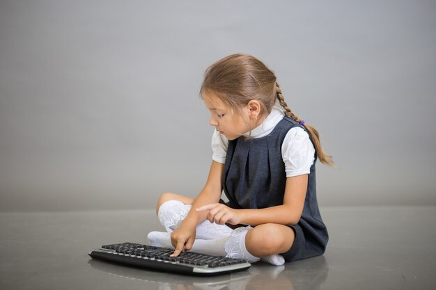 La ragazza in uniforme scolastica si siede e lavora alla tastiera