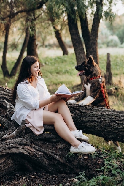 La ragazza in vestiti bianchi si siede su un albero nella foresta e legge un libro