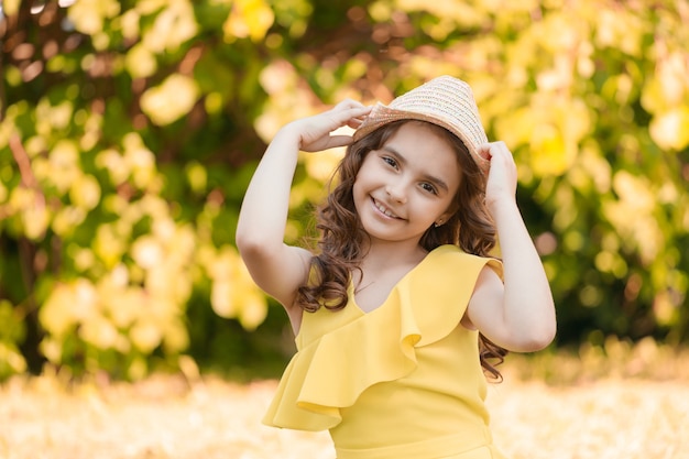 La ragazza in vestiti gialli e cappello si siede sull'erba nel parco in estate. Foto di alta qualità