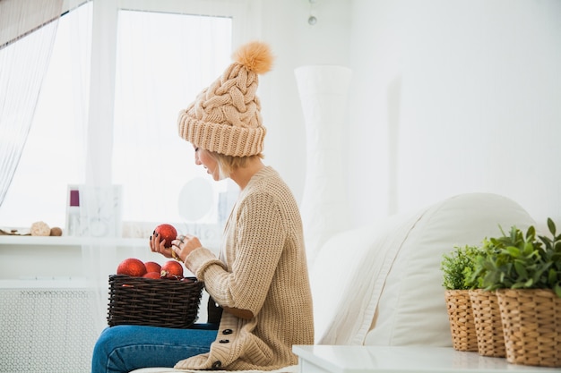 La ragazza in vestiti lavorati a maglia accoglienti tiene il cestino della decorazione delle palle di natale