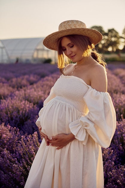 La ragazza incinta con un cappello nel campo di lavanda su un tramonto