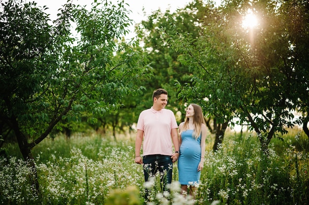 La ragazza incinta e suo marito sono felici di tenersi per mano, stare all'aperto sulla superficie del giardino con alberi