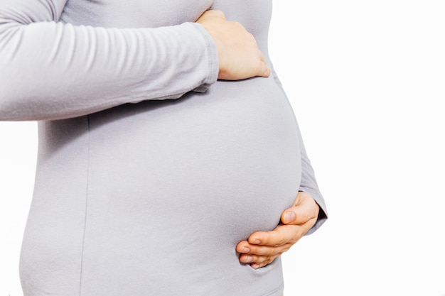 La ragazza incinta tiene uno stomaco in un vestito grigio su un bianco