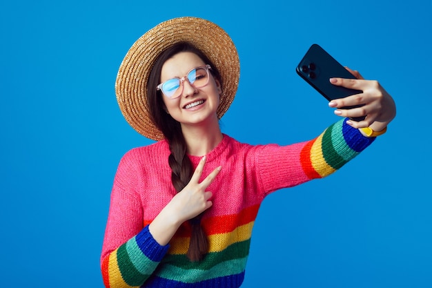 La ragazza indossa un maglione arcobaleno si fa il selfie con il cellulare mentre mostra il gesto di pace