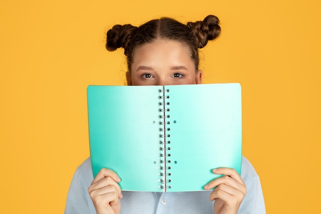 La ragazza intelligente europea adolescente sorridente copre il viso con il libro si prepara a testare