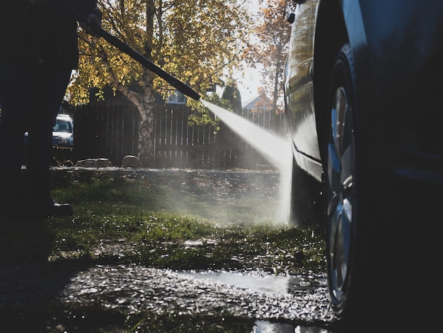 La ragazza lava l'auto a casa vicino al garage usando un'idropulitrice