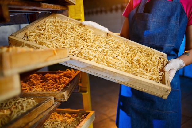 La ragazza lavora alla produzione di spaghetti. Fare le tagliatelle. Pastificio. Fase di produzione della pasta. Tagliatelle crude. Operaio con una scatola di pasta.