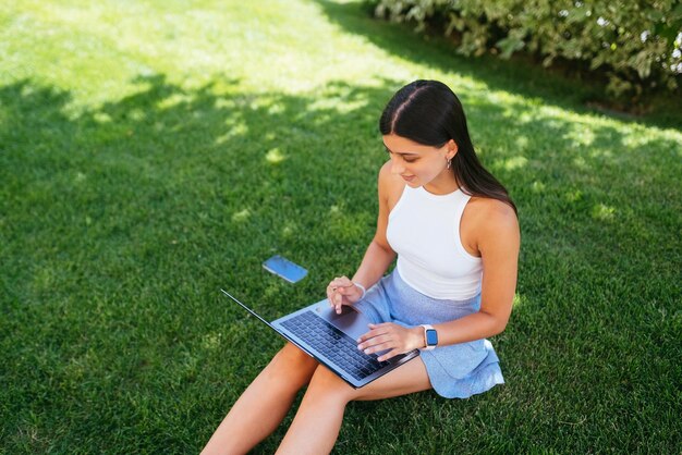 La ragazza lavora con un computer portatile seduto sul prato