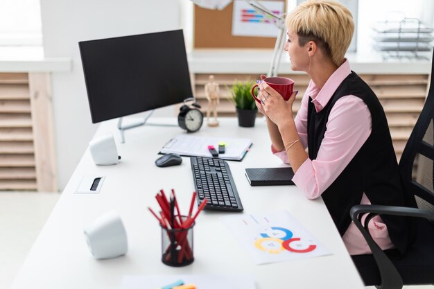 La ragazza lavora in ufficio al computer e tiene in mano una tazza.