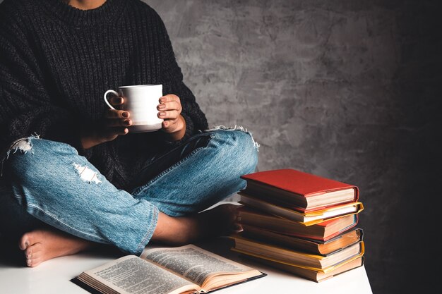 La ragazza legge libri, studia, sviluppa con una tazza di caffè su un tavolo bianco e uno sfondo grigio.