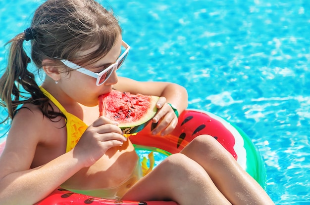 La ragazza mangia l'anguria in un'anguria gonfiabile in piscina