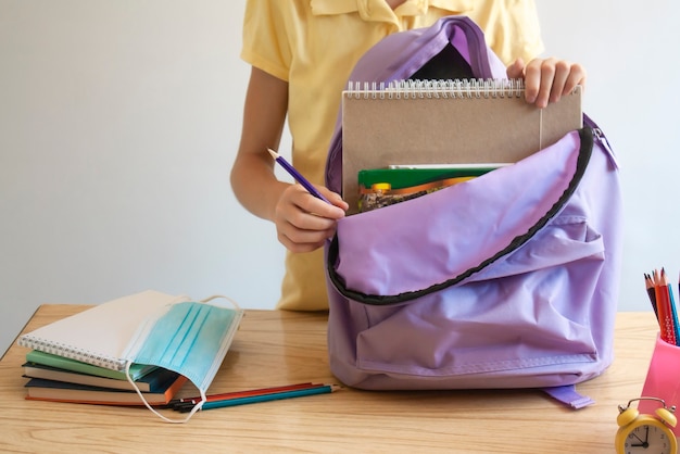 La ragazza mette il materiale scolastico e una maschera protettiva in uno zaino