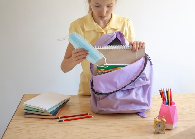 La ragazza mette il materiale scolastico e una maschera protettiva in uno zaino