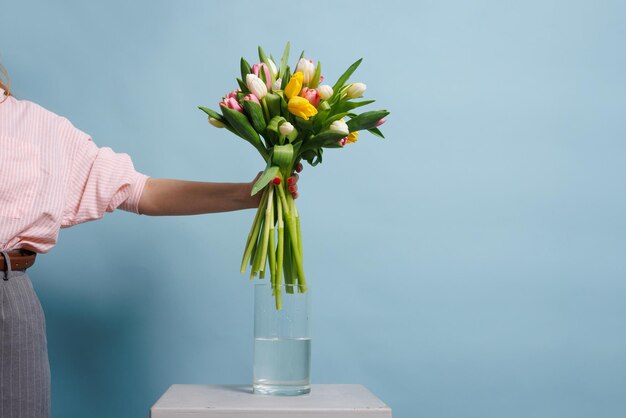 la ragazza mette un bouquet di tulipani in acqua su uno sfondo blu pulito