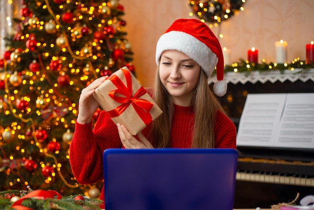 La ragazza mostra il suo regalo a un amico mentre ha una videochiamata Concetto di relazione a distanza di decorazione festosa atmosfera natalizia