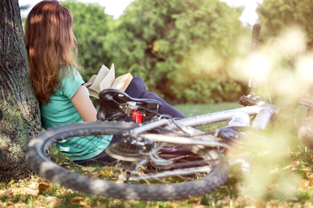 La ragazza nel parco si siede sotto un albero e legge un libro. accanto c'è una bicicletta e uno zaino