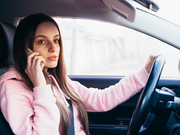 La ragazza nel pietà rosa parla al telefono mentre si siede in un'automobile.