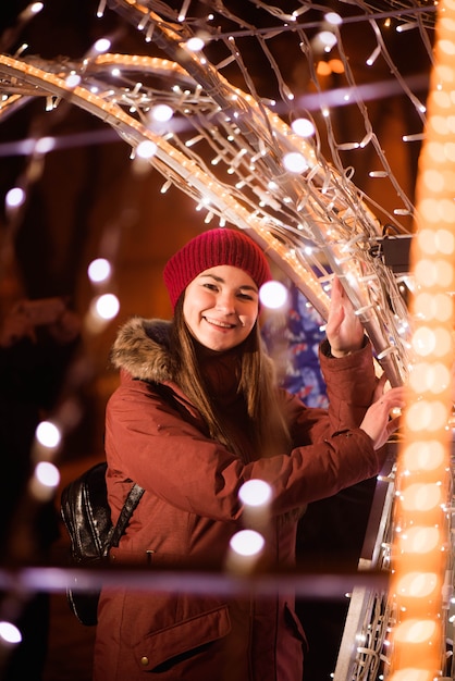 La ragazza nell'inverno copre sopra il fondo delle luci, vicino alle luci dell'albero di Natale