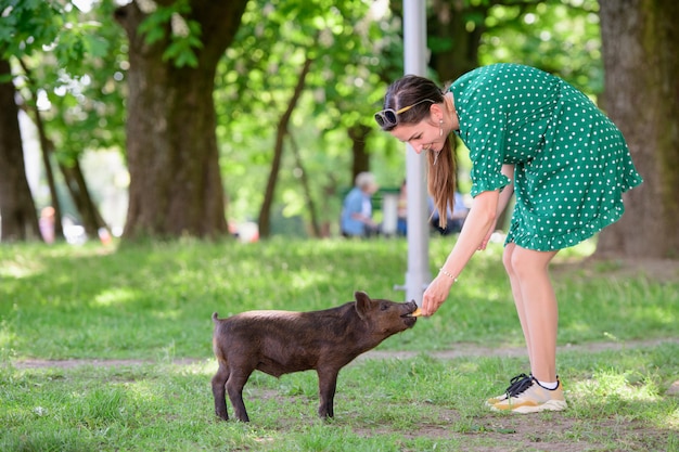 La ragazza nutre un maialino. in un prato verde. Il concetto di sostenibilità, amore per la natura, rispetto per la pace e amore per gli animali. Ecologico, biologico, vegano, vegetariano