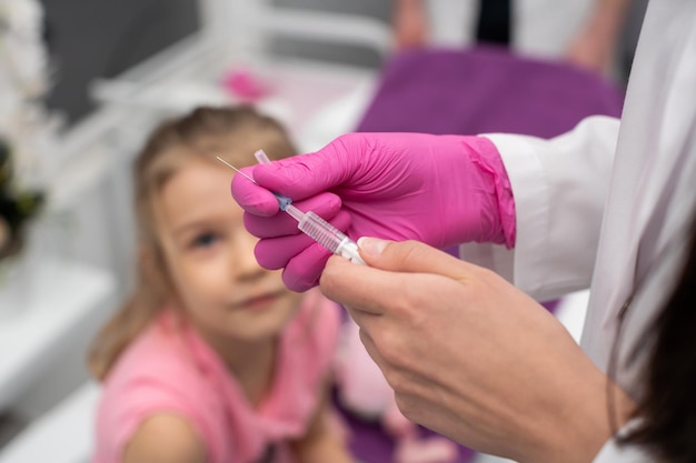 La ragazza osserva con curiosità mentre il medico prepara la siringa per l'iniezione vaccino preventivo per i bambini piccoli