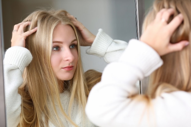 La ragazza osserva il riflesso allo specchio, raddrizza i capelli.