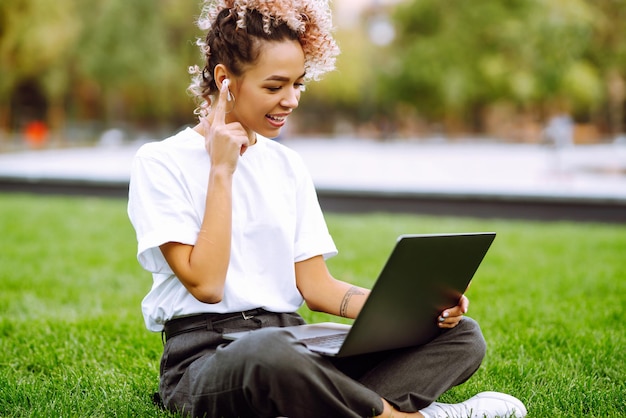 La ragazza parla durante una videochiamata con i colleghi durante un briefing online su un computer portatile moderno seduto nel parco