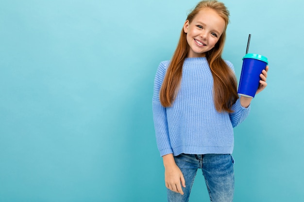 La ragazza piacevole allegra posa con una tazza di caffè su un fondo blu