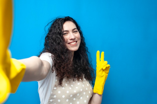 la ragazza più pulita in uniforme e guanti per la pulizia prende selfie e mostra un gesto di pace